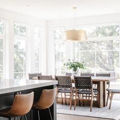 a kitchen island with chairs and a table in front of large windows that look out onto the woods