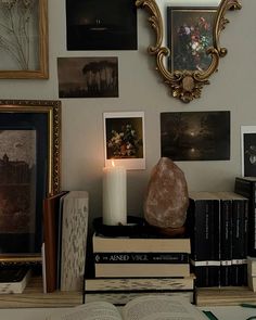 a table topped with books and a lit candle next to pictures on the wall behind it