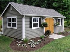 a small gray shed with yellow door and windows on the side, surrounded by flowers