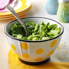 a bowl filled with broccoli sitting on top of a yellow napkin next to plates