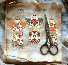 three paper doll angels with scissors on a piece of parchment paper next to some other items