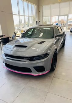 a gray car is parked in a showroom with other cars behind it and on the floor