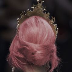 a woman with pink hair and a crown on her head is seen from the back