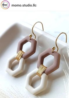 two tone hexagon earrings with gold accents on a white plate next to feathers