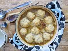 a pot filled with meatballs sitting on top of a wooden table next to spoons