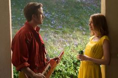 a man and woman standing next to each other in front of a window with flowers