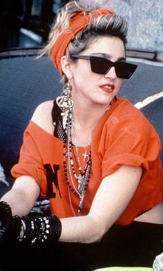 a woman in an orange top and black sunglasses sitting on the back of a car