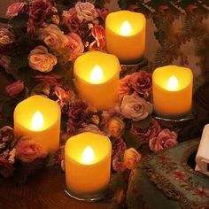 five lit candles sitting on top of a wooden table next to flowers and a clock