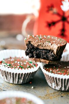 three chocolate cupcakes with sprinkles on them sitting on a table