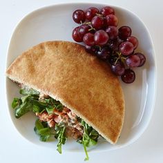 a white plate topped with a sandwich and grapes