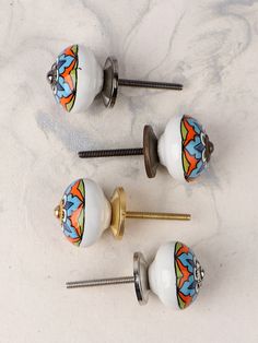 three decorative knobs and two screws on a white marble counter top with colorful designs