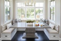 a table and benches in a room with white walls, windows, and wood flooring