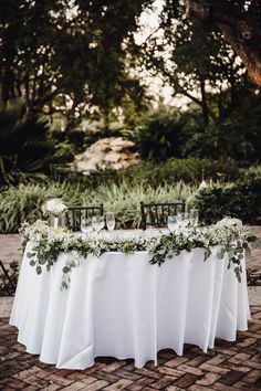 a table with white linens and greenery is set up for an outdoor wedding