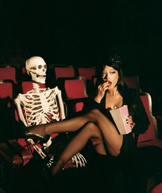 a woman sitting on a red chair in front of a skeleton holding a popcorn box