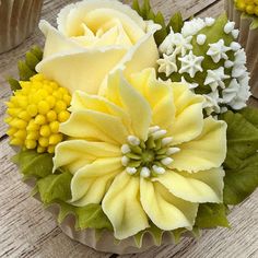 yellow and white flowers in a vase on a wooden table with other cupcakes