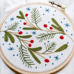 a close up of a embroidery on a white cloth with red berries and green leaves