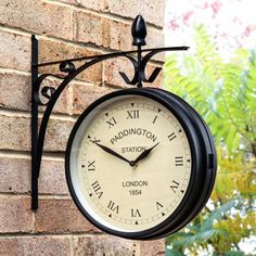 a black and white clock hanging from the side of a brick building with trees in the background