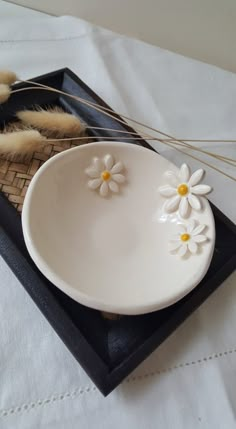 a white plate with daisies on it sitting on a black tray next to feathers