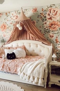 a white bed sitting next to a wall covered in pink and orange flowers with a black cat laying on top of it