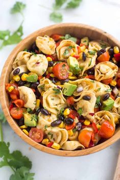 a wooden bowl filled with pasta salad on top of a white counter next to cilantro