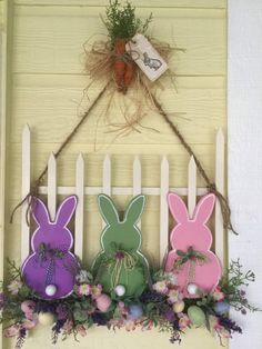 some bunny decorations are hanging on the wall next to a white picket fence with grass and flowers