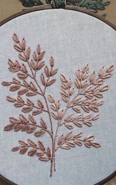 a close up of a embroidery on a piece of cloth with an embroidered plant in the middle