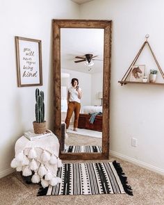 a woman standing in front of a mirror with a rug on the floor next to it