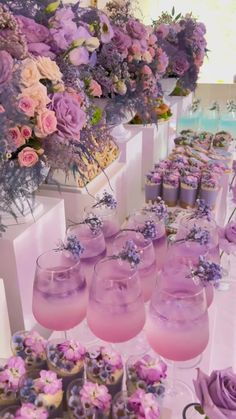 there are many cupcakes on the table with purple frosting and flowers in vases