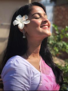 a woman with long black hair wearing a white flower in her hair and looking up at the sky