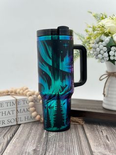 a blue and green travel mug sitting on top of a wooden table next to flowers