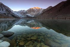 a mountain lake surrounded by rocks and snow covered mountains in the distance, at sunset