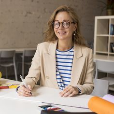 a woman sitting at a table with a pen and paper in her hand while smiling