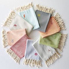 six different colors of handkerchiefs on a white tablecloth with tassels around them