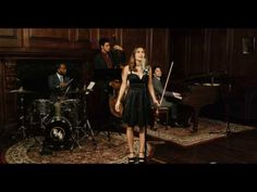 a woman standing in front of a piano and other people playing music on the stage