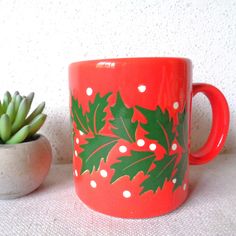 a red coffee mug sitting next to a succulent plant on a white surface