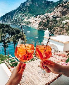 two people holding up wine glasses with water in the background