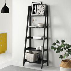 a black leaning shelf next to a yellow cabinet and potted plant in a white room