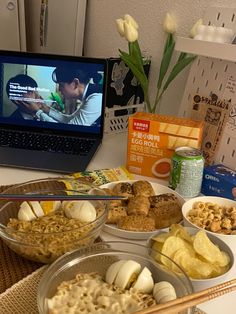 an open laptop computer sitting on top of a table next to bowls of food and snacks