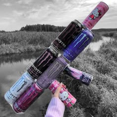 a person holding several different types of water bottles in front of a body of water