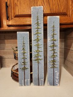 two wooden signs with pine trees painted on them sitting on a kitchen counter next to a potted plant