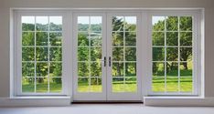 an empty room with double doors and windows overlooking the green grass field in the distance