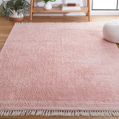 a pink rug with fringes on the floor in front of a wooden shelf and potted plant