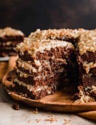 a chocolate cake with coconut frosting is cut in half on a wooden platter