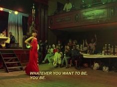 a woman in a red dress standing on top of a wooden floor next to a group of people