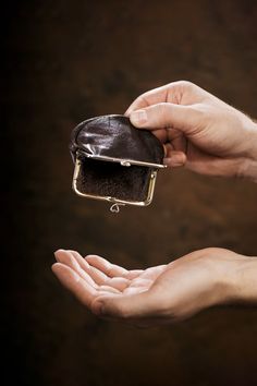 two hands holding a small purse in the palm of someone's hand, against a dark background