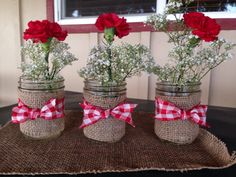 three mason jars with red flowers and baby's breath are sitting on a table