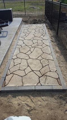 a cement walkway in the middle of a dirt field next to a fence and bench