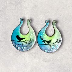 pair of earrings with birds on tree branch and water drops painted on them, hanging from hooks