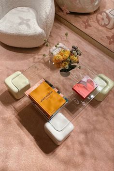 a glass table with books and flowers on it in a room that has pink carpet