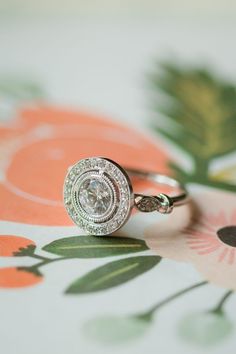 a diamond ring sitting on top of a flowered tablecloth with an orange and white background